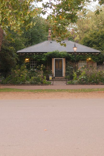 A detailed, high-resolution image of a small front garden in NW1, showing neatly trimmed grass forming a lush green lawn bordered by well-maintained flower beds. The flower beds contain a variety of p